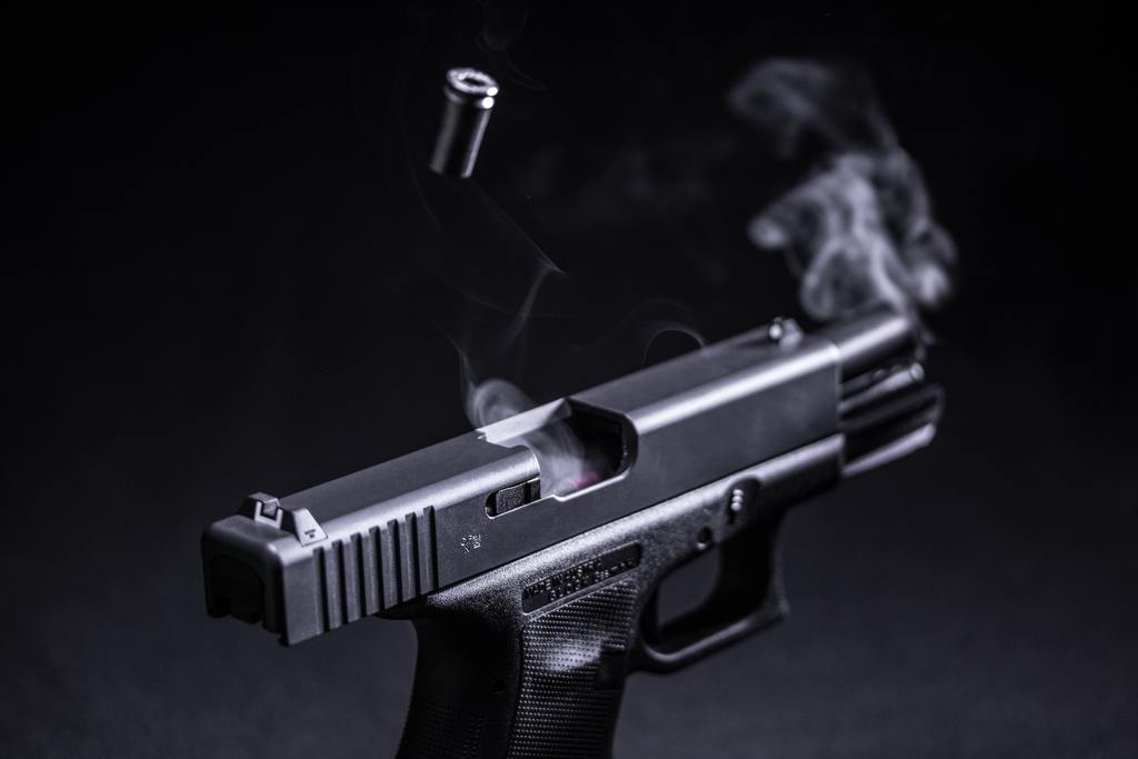 A black hand gun in front of a black background with smoke and bullets coming out of it