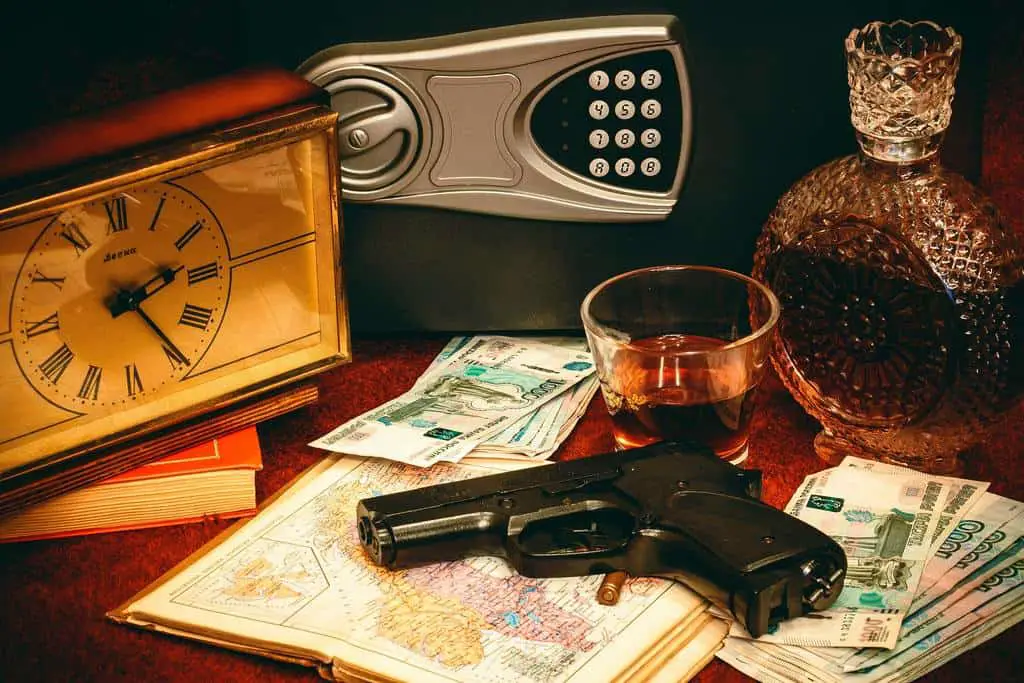 Hand gun beside a bottle and a glass of whisky, a vault and a clock