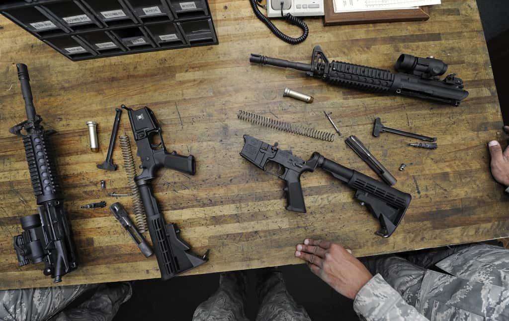 A group of black firearms are laid on top of a wooden table