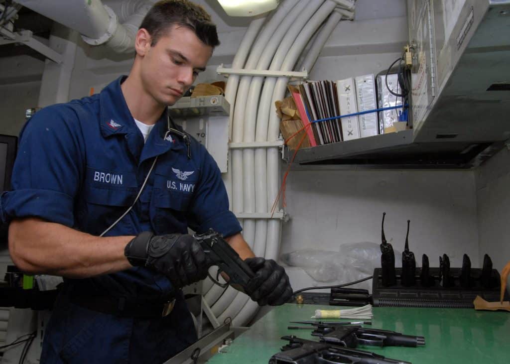 A marine in a blue jumpsuit wiping down firearms