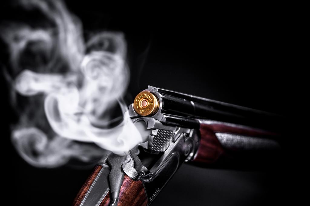 A loaded gun is smoking from the back infront of a black background