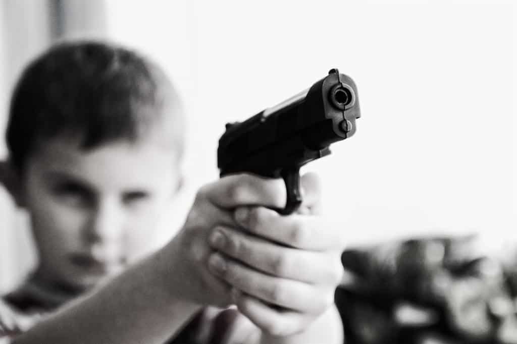 Kid holding up a gun with his finger on the trigger