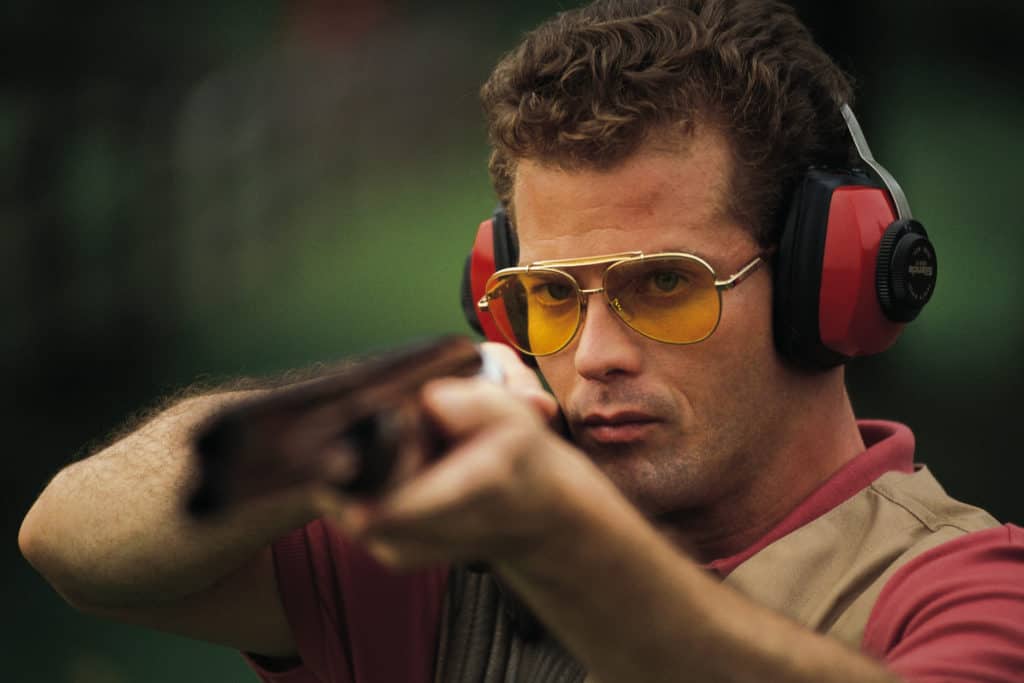 Man wearing full shooting gear while about to fire a gun in a shooting range