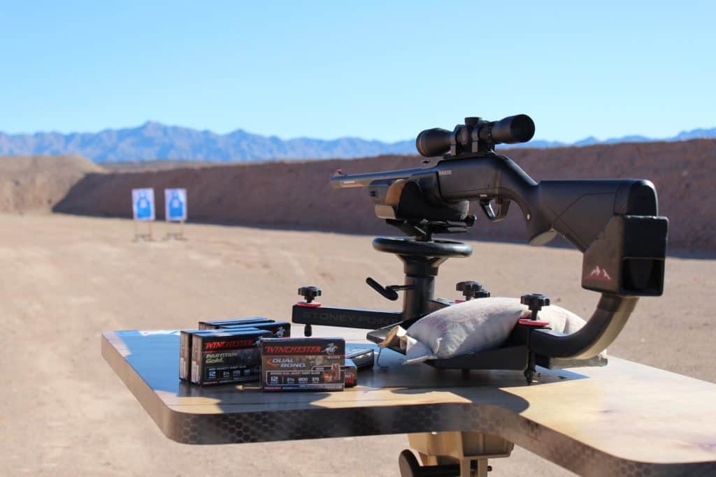 A stationary rifle, boxes of ammunition at an outdoor gun range