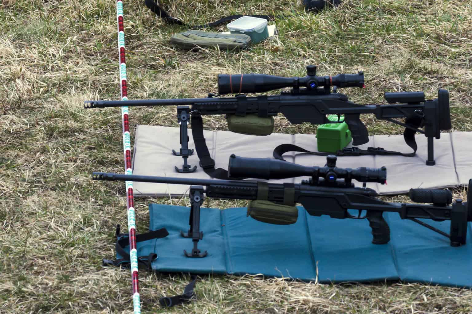 Military rifles aims at a target while being cushioned by a shooting mat on the ground