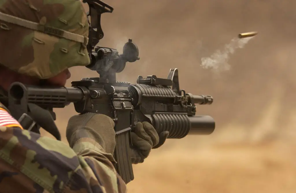 a man wearing a camo and firing a rifle