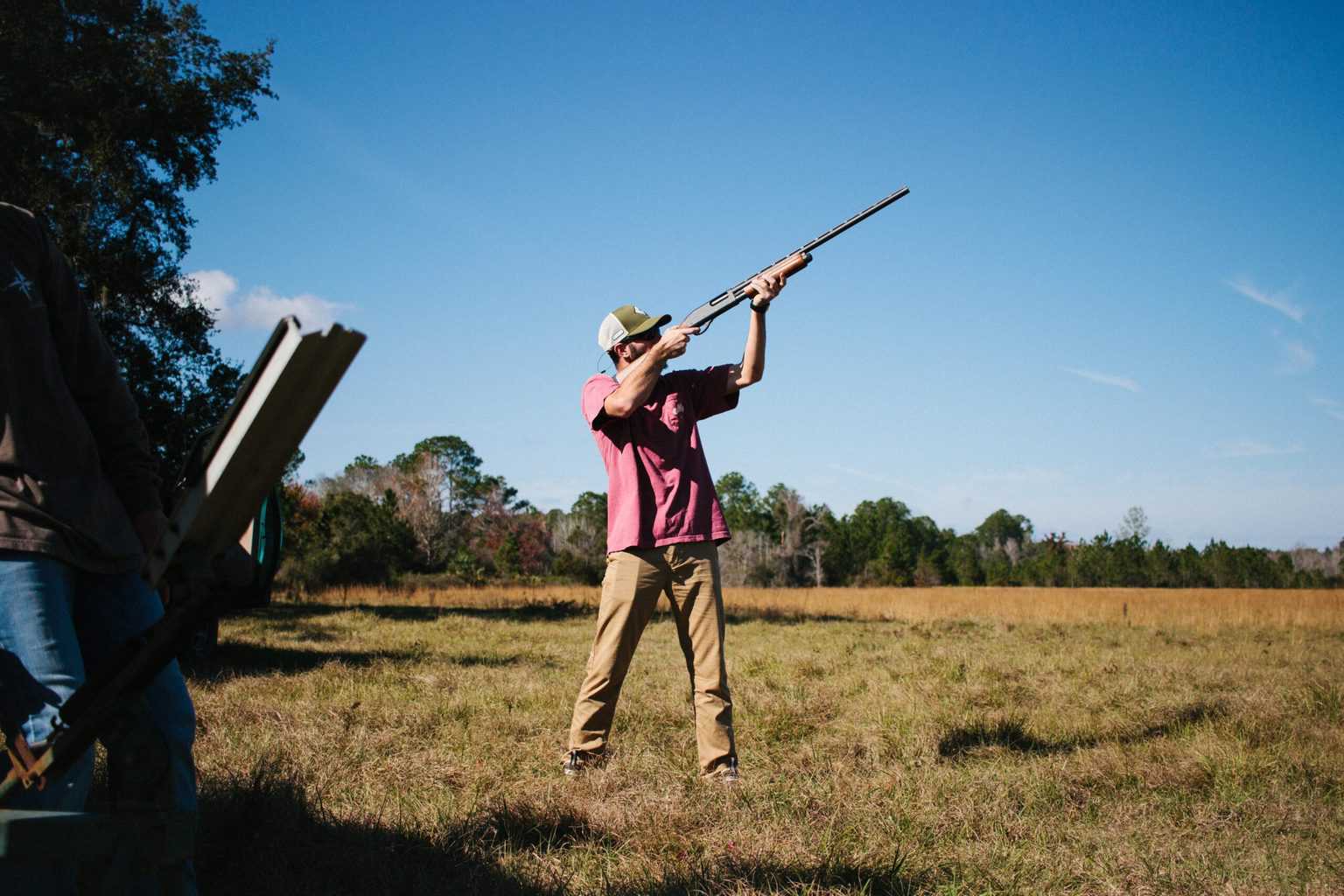 A man aiming a shotgun to the sky in an open field