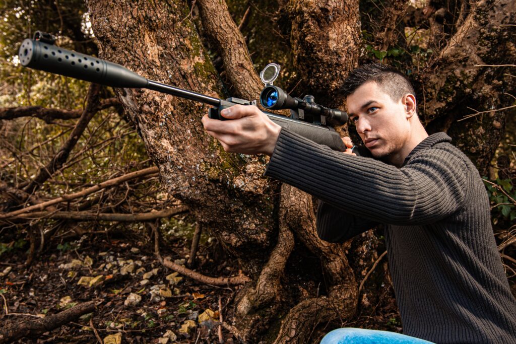 A man holding a sniper beside a tree