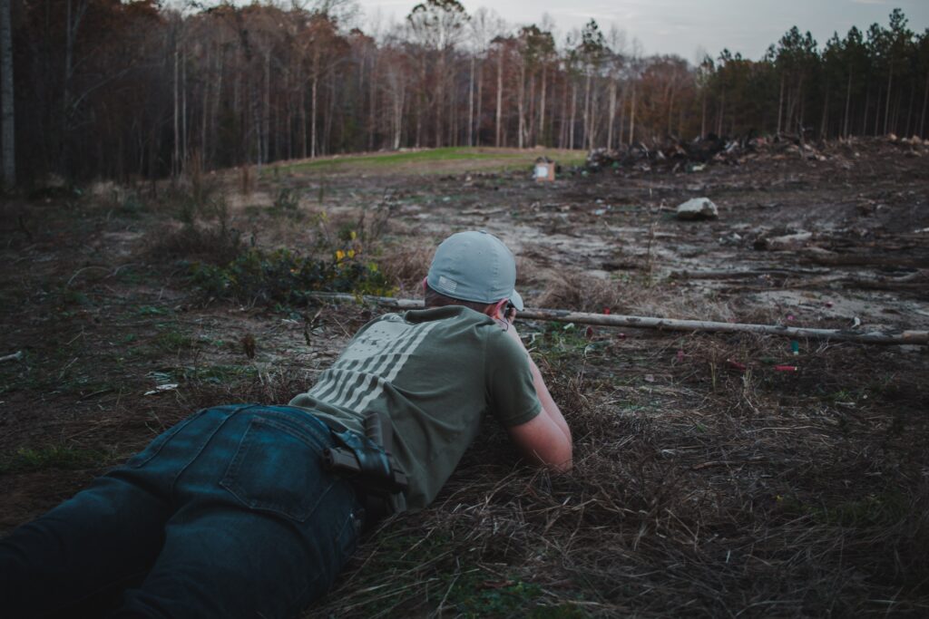 person laying down shooting gun in an open area