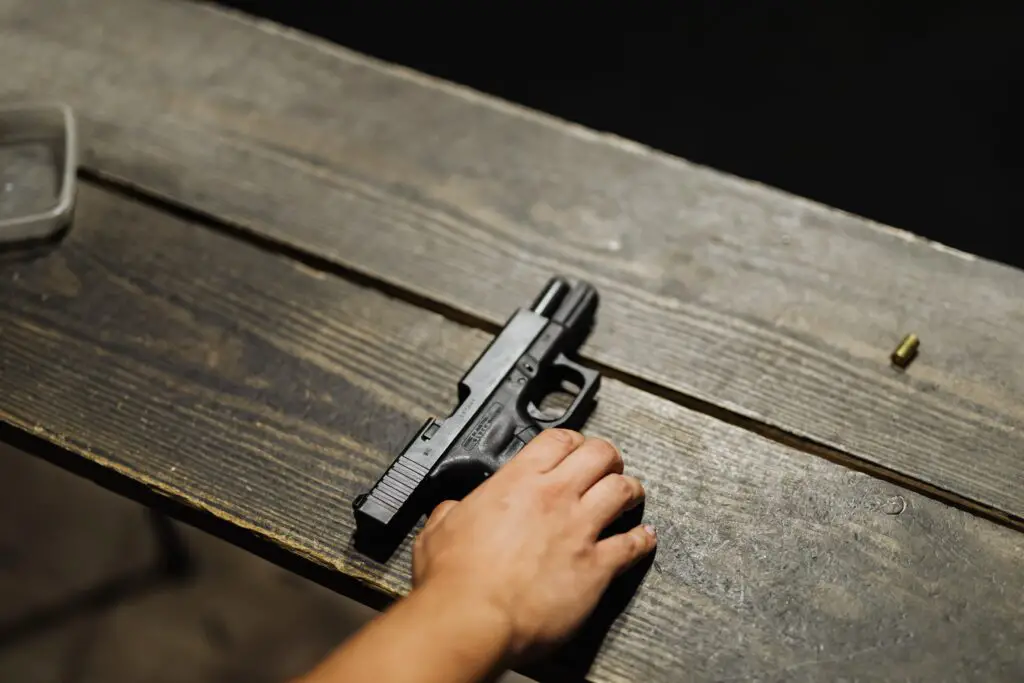 hand holding down a pistol on a wooden table