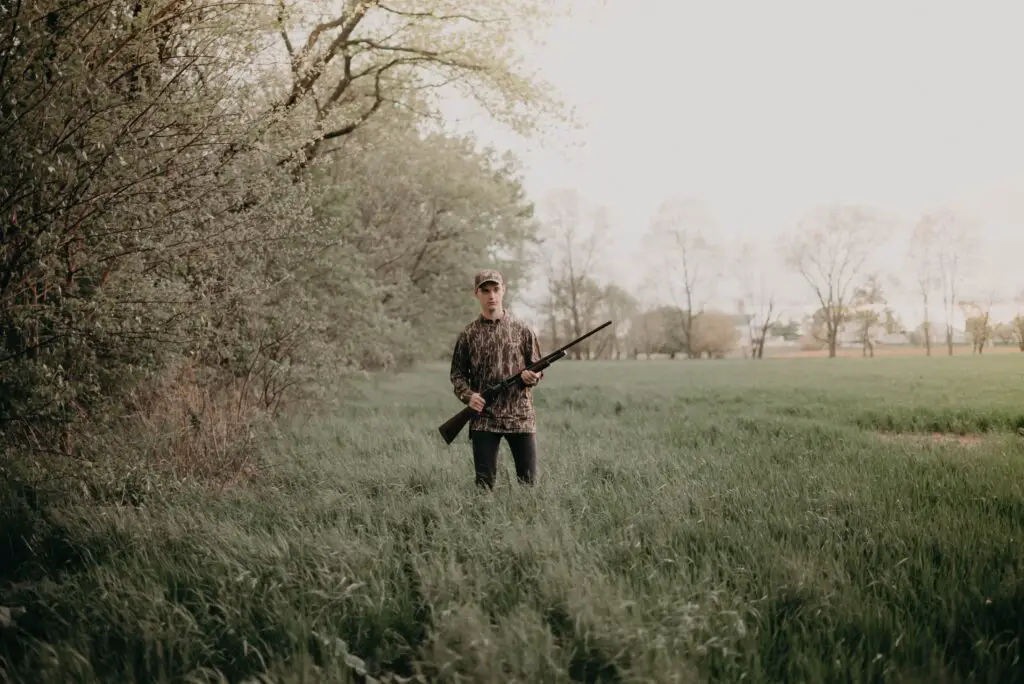 person holding a rifle in an open area with a lot of grass