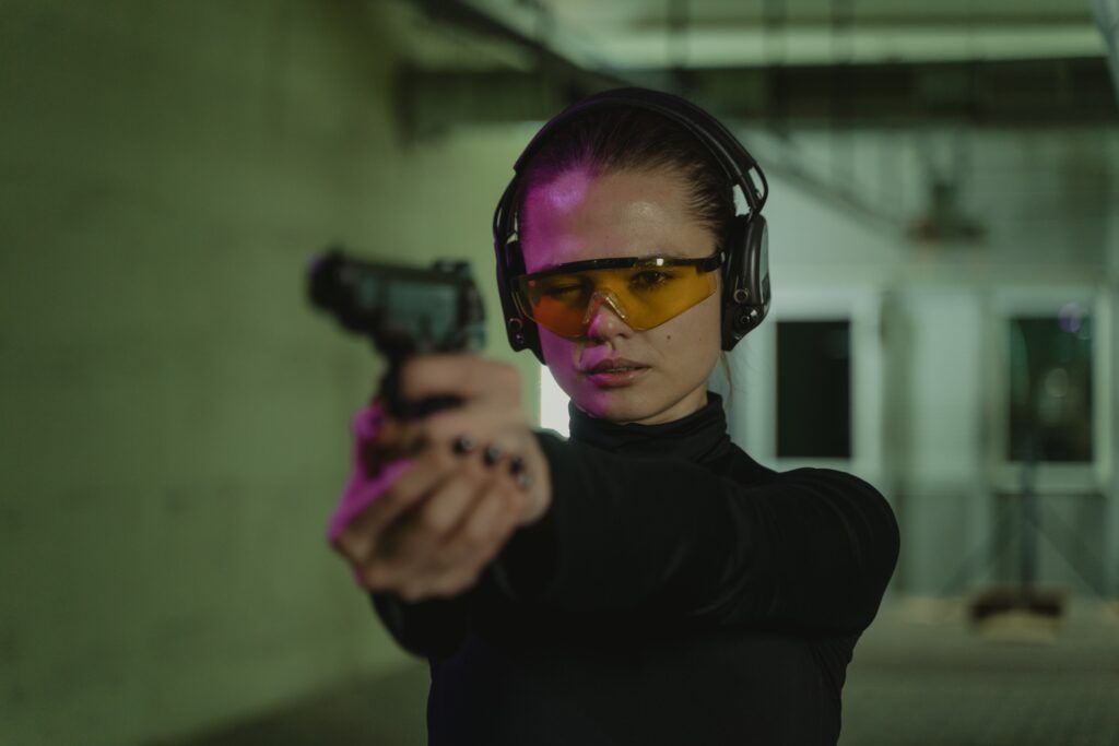 woman in black wearing protective gear while holding a gun practicing shooting