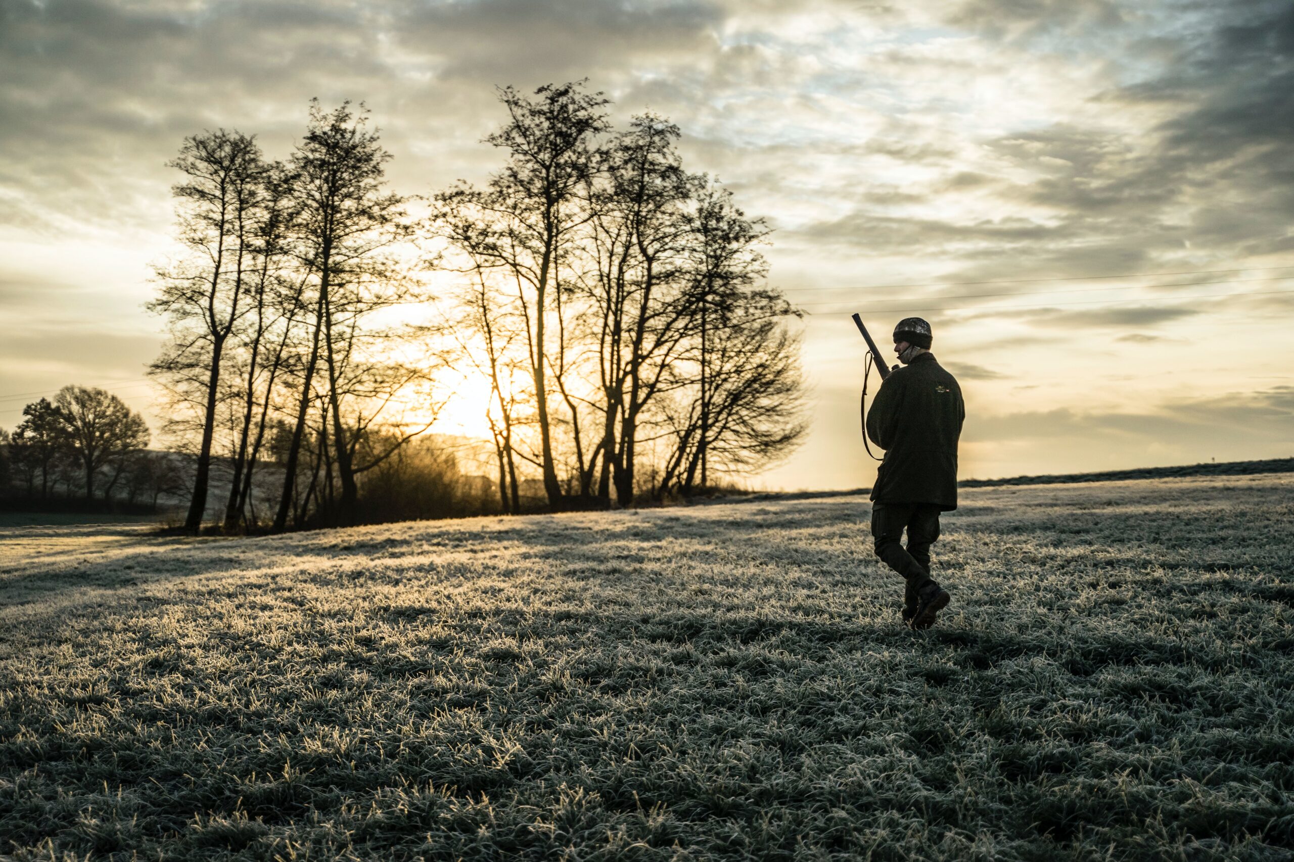 Man wearing a jacket standing on a grass field holding a rifle