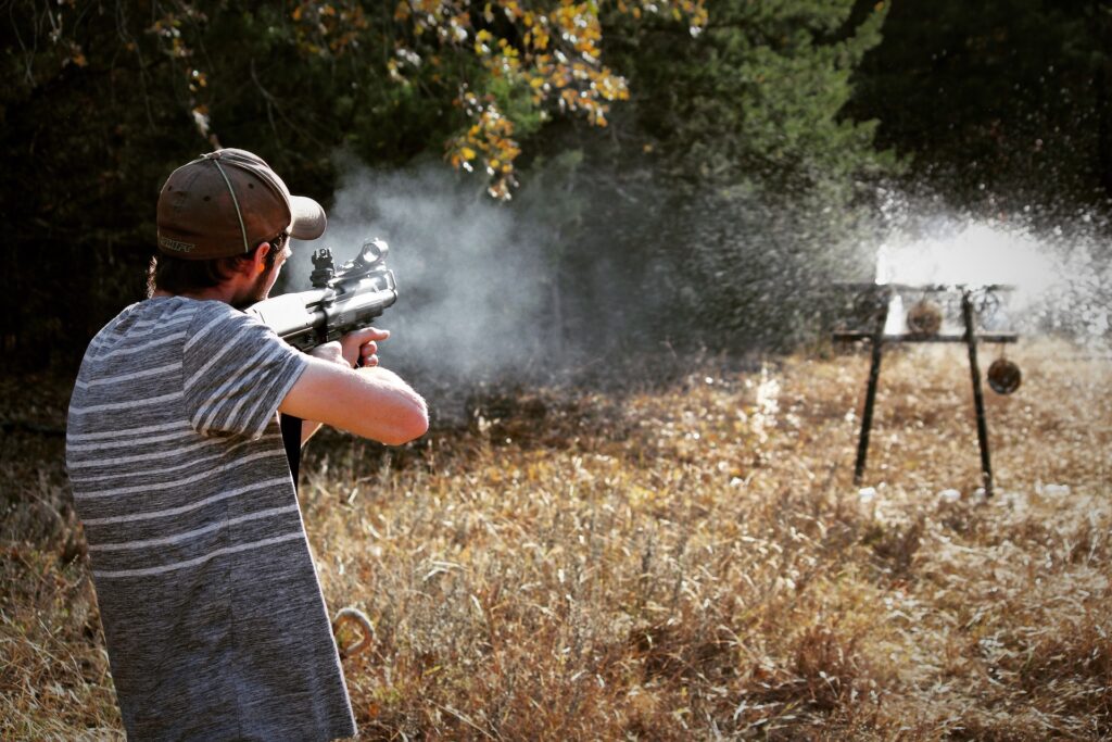 Guy wearinga cap and gray striped shirt shooting a target with a rifle