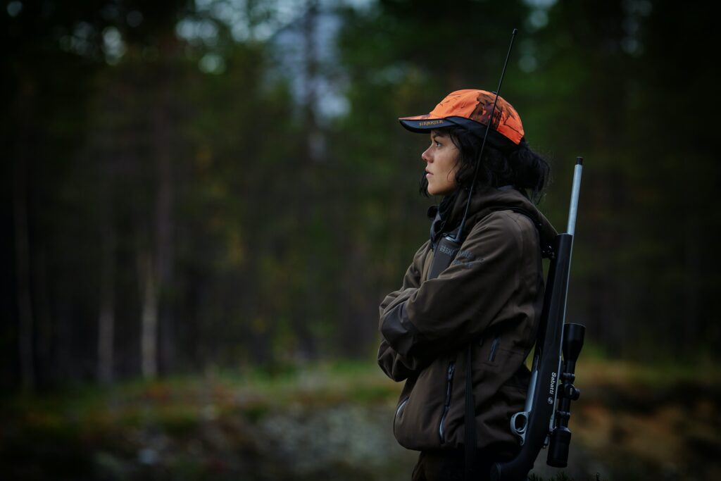 A person wearing an orange cap and carrying a sniper hunting rifle