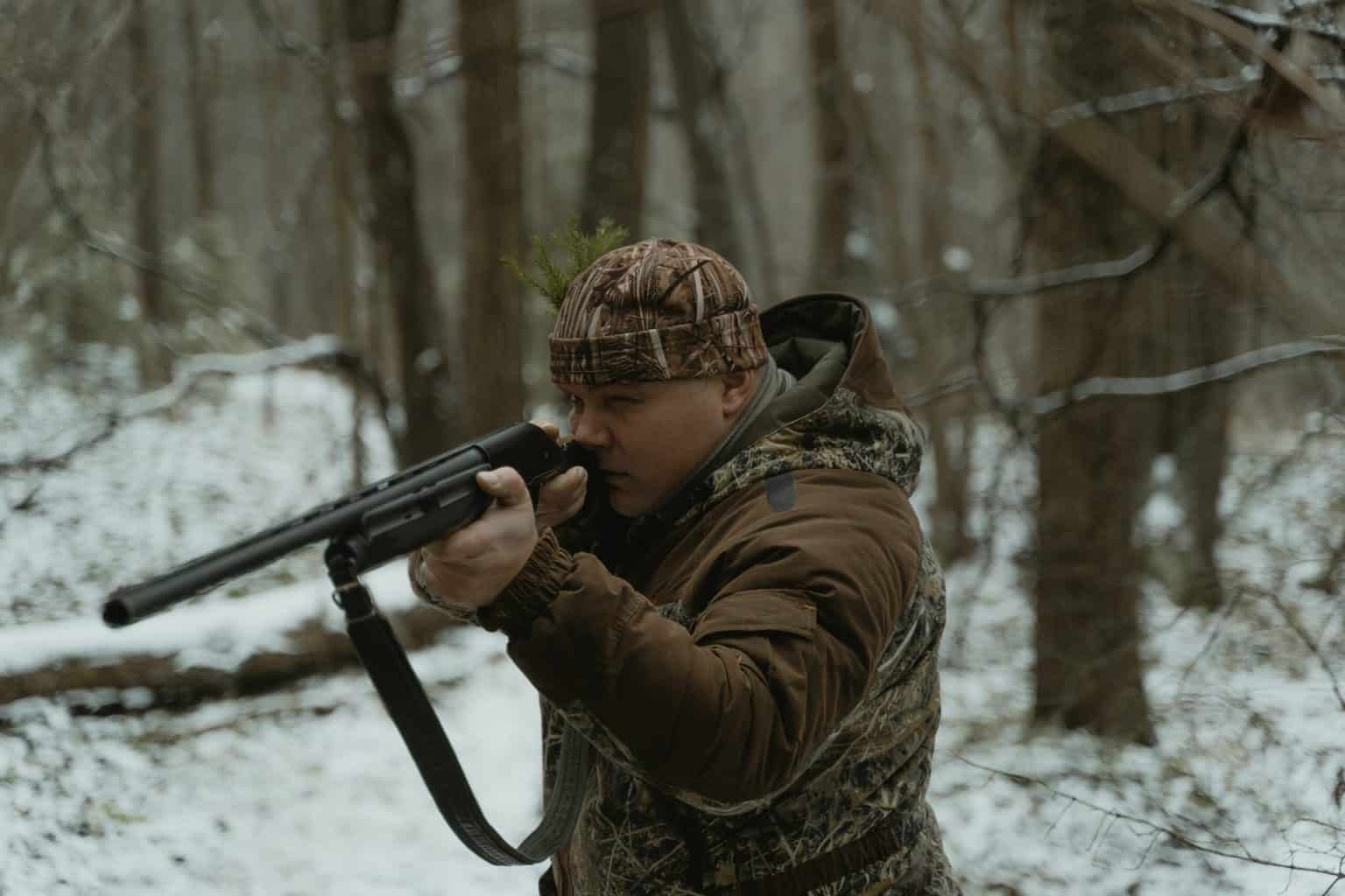 A person wearing a brown camo while aiming with a long gun