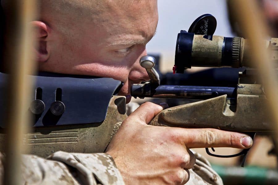 Man holding a rifle while looking at his scope