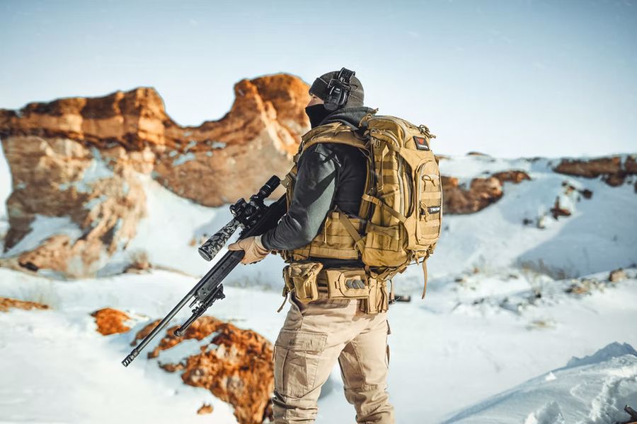 Man with a range bag while holding a rifle outdoors