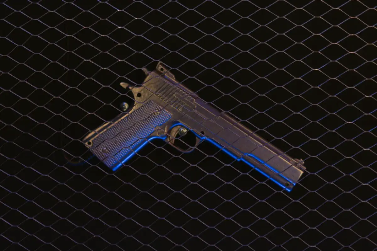A black pistol placed on a black stainless wire screen with a black background