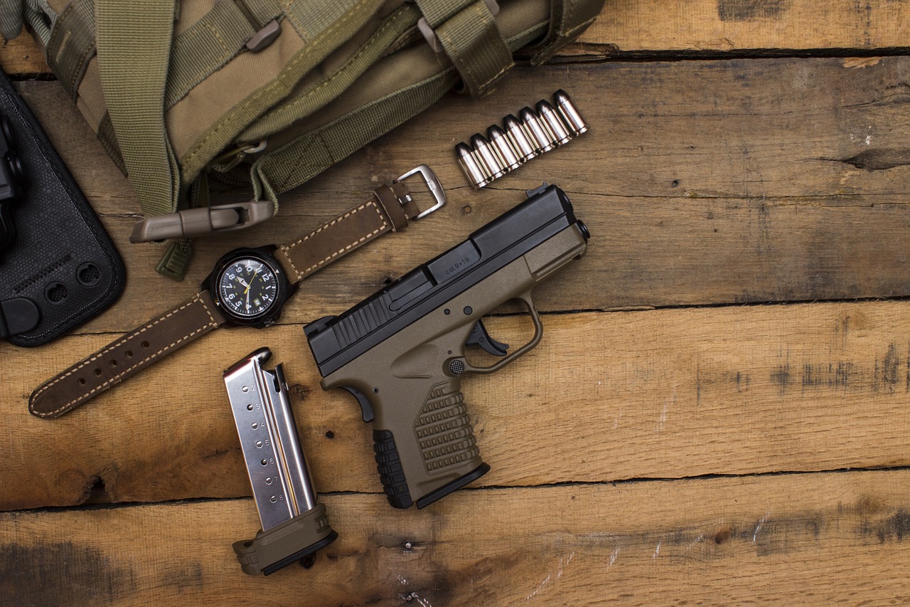 A black and brown handgun pistol beside a brown watch and green bag on a brown wooden table