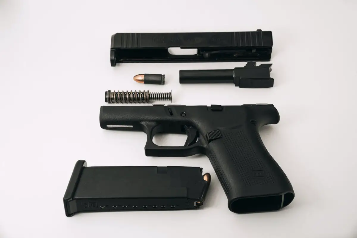 Disassembled black semi-automatic pistol with loaded magazine placed on a white surface