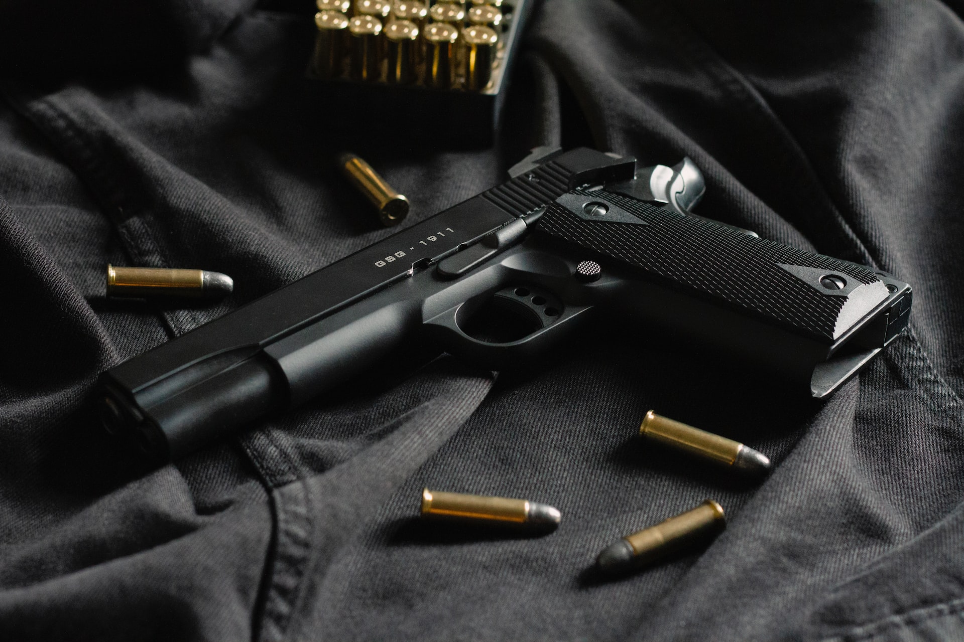 Black semi-automatic pistol surrounded by gold bullets placed on a black cloth