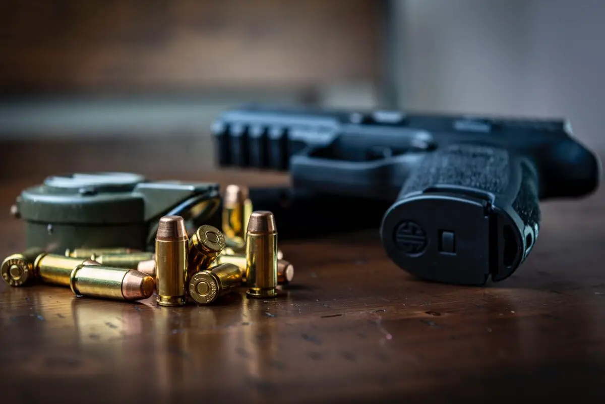 A black handgun near golden bullets on top of a brown wooden table