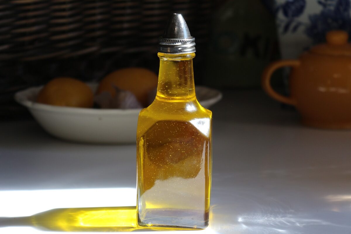 A glass oil dispenser with a silver tip filled with oil on top of a white table