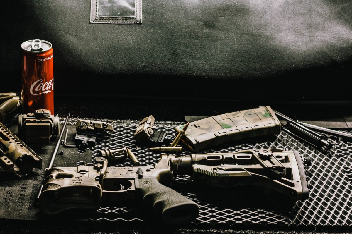 Rifle with a camouflage design near a can of Coca-Cola on top of a black steel table