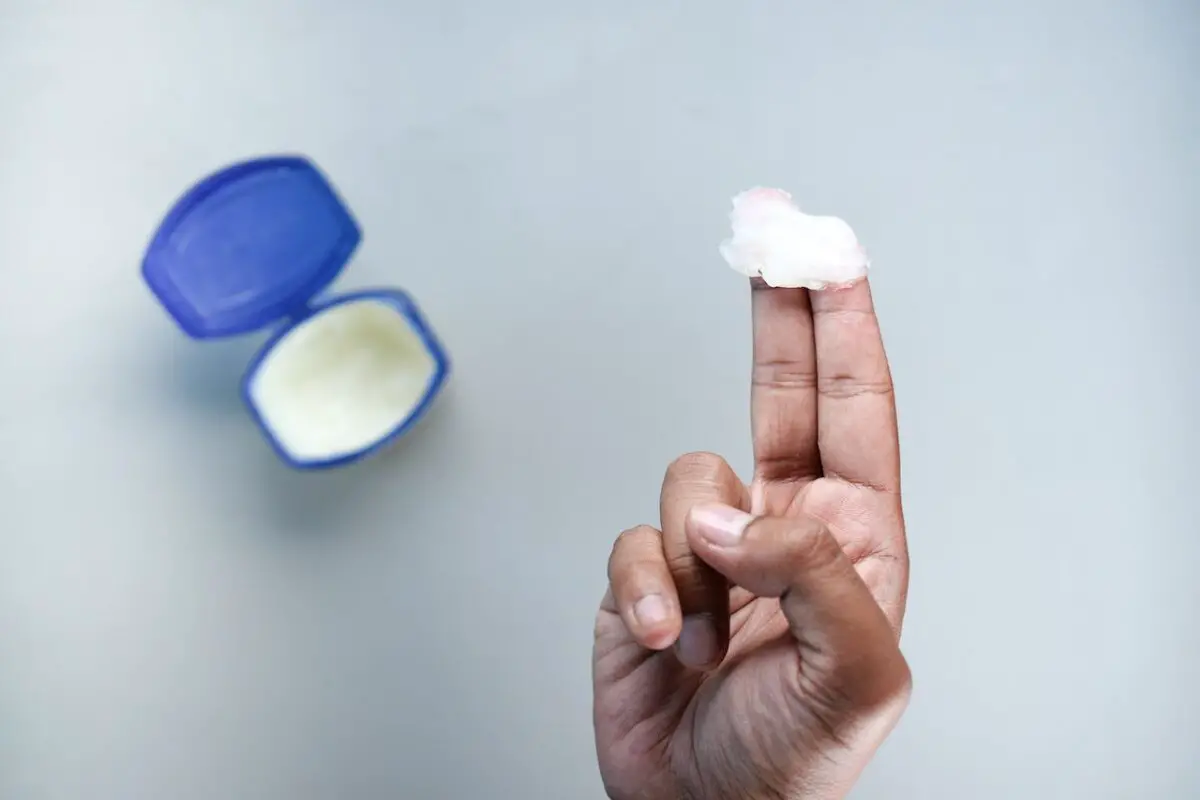A person using two fingers to get vaseline on the blue container on a white surface